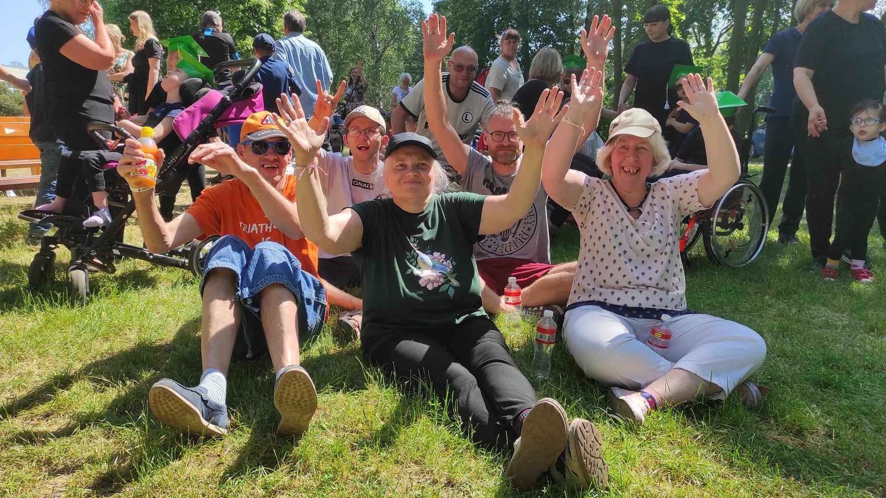 Pensjonariusze siedzą na trawie z podniesionymi do góry rękami